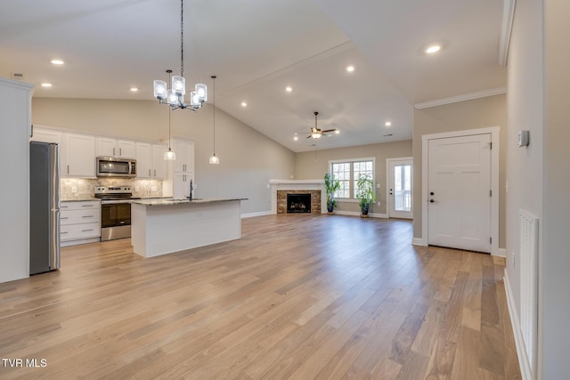 kitchen with white cabinetry, hanging light fixtures, stainless steel appliances, backsplash, and a center island with sink