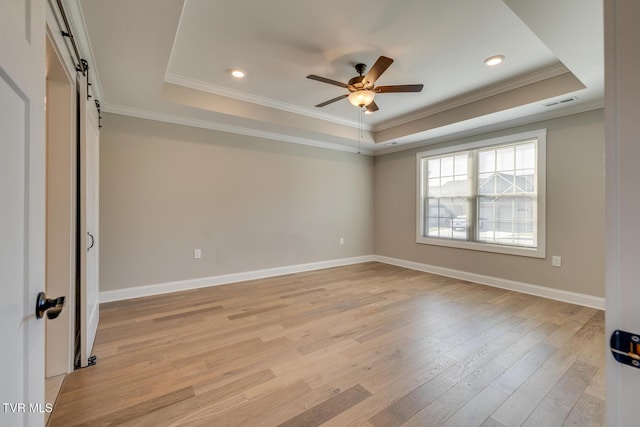 spare room featuring a barn door, light hardwood / wood-style floors, and a tray ceiling