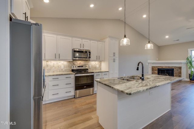 kitchen featuring decorative backsplash, appliances with stainless steel finishes, pendant lighting, white cabinets, and an island with sink