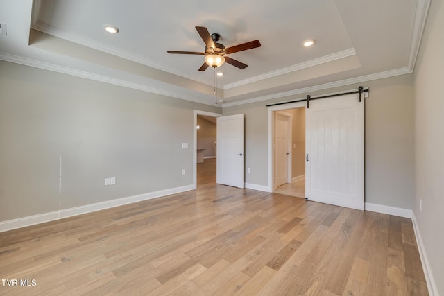 unfurnished bedroom featuring ceiling fan, a barn door, crown molding, and a tray ceiling