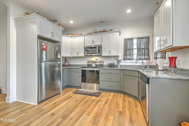 kitchen featuring appliances with stainless steel finishes, light wood-type flooring, light stone counters, gray cabinetry, and sink