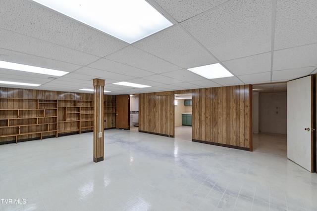 basement featuring a paneled ceiling and wood walls