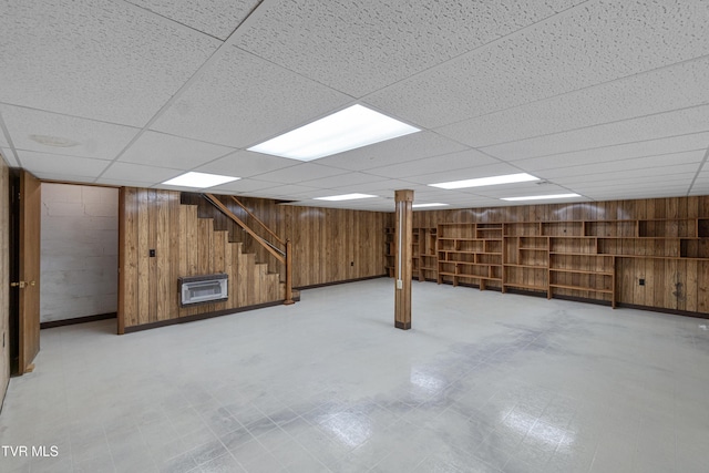 basement featuring a paneled ceiling, heating unit, and wood walls