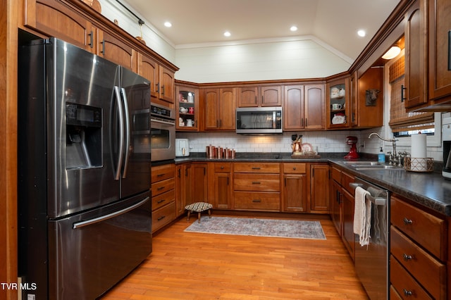 kitchen featuring sink, backsplash, lofted ceiling, appliances with stainless steel finishes, and light wood-type flooring