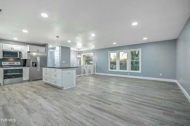 kitchen with dark countertops, light wood finished floors, backsplash, appliances with stainless steel finishes, and white cabinets