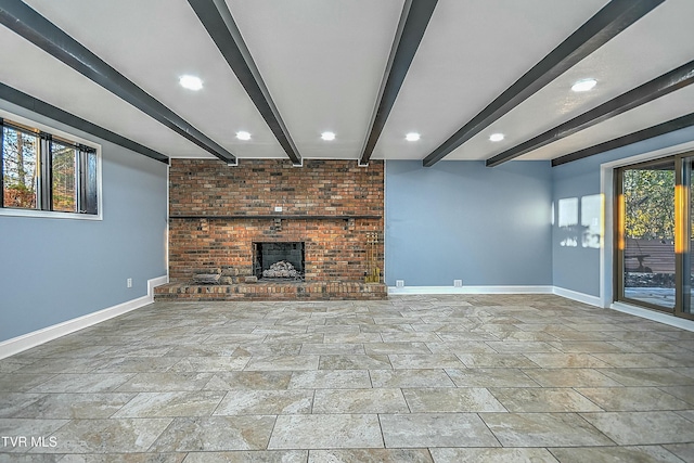 unfurnished living room featuring a wealth of natural light, beam ceiling, and a brick fireplace