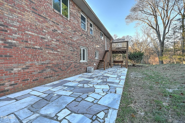 exterior space with brick siding, a wooden deck, stairs, and a patio