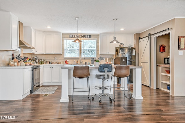 kitchen with white cabinetry, a breakfast bar area, hanging light fixtures, a barn door, and wall chimney range hood