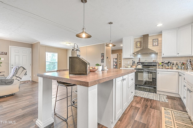 kitchen featuring wall chimney range hood, white cabinets, black range with electric stovetop, and a kitchen island