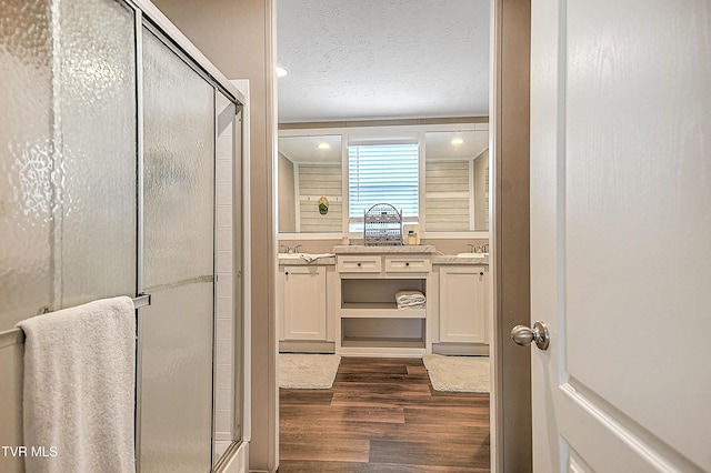 bathroom with vanity, a shower with door, wood-type flooring, and a textured ceiling