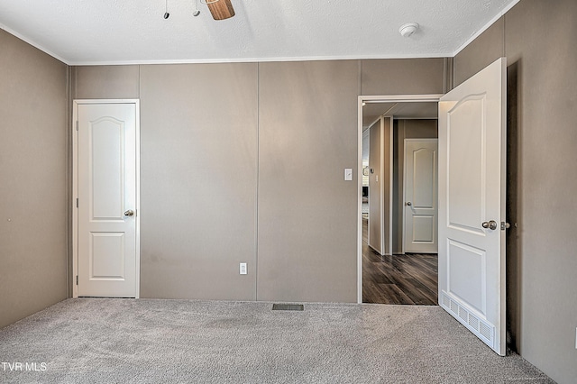 unfurnished bedroom featuring ceiling fan, a closet, a textured ceiling, and dark colored carpet