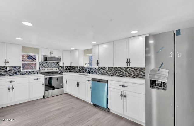 kitchen with white cabinets, sink, light hardwood / wood-style flooring, appliances with stainless steel finishes, and tasteful backsplash