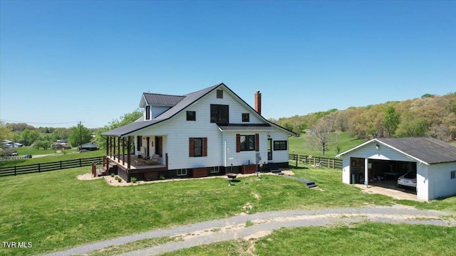 rear view of property with covered porch, a garage, an outbuilding, and a lawn