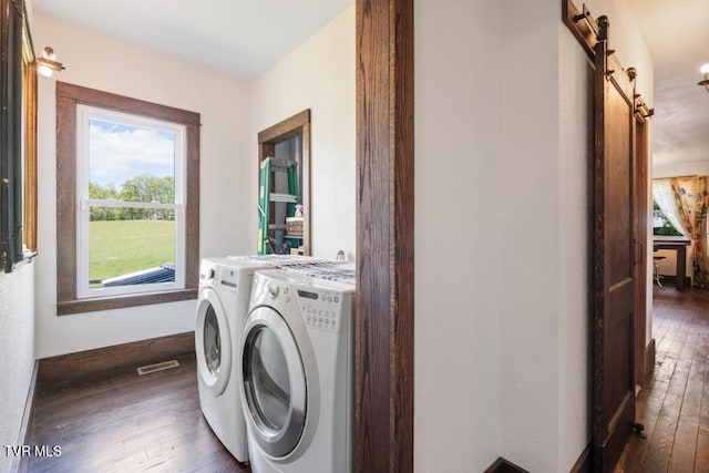 clothes washing area featuring washer and dryer, a barn door, and dark hardwood / wood-style flooring