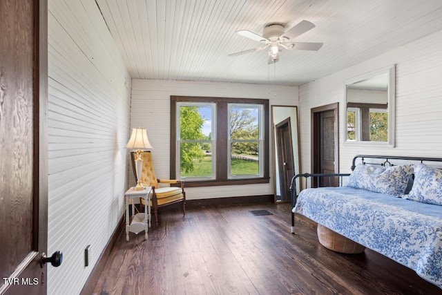 bedroom featuring multiple windows, wooden walls, ceiling fan, and dark wood-type flooring