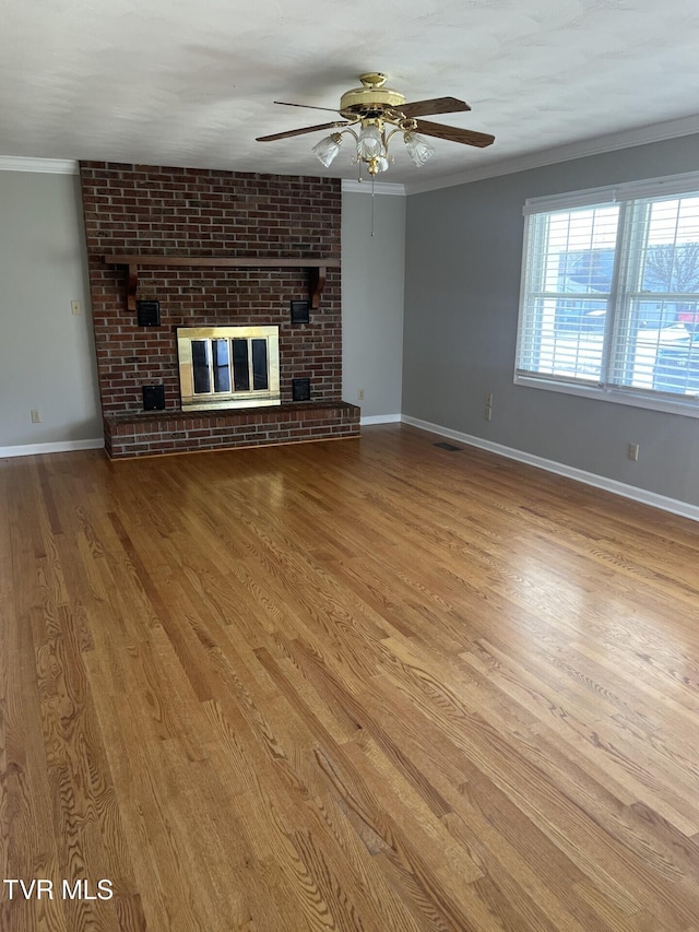 unfurnished living room featuring a brick fireplace, baseboards, ornamental molding, and wood finished floors