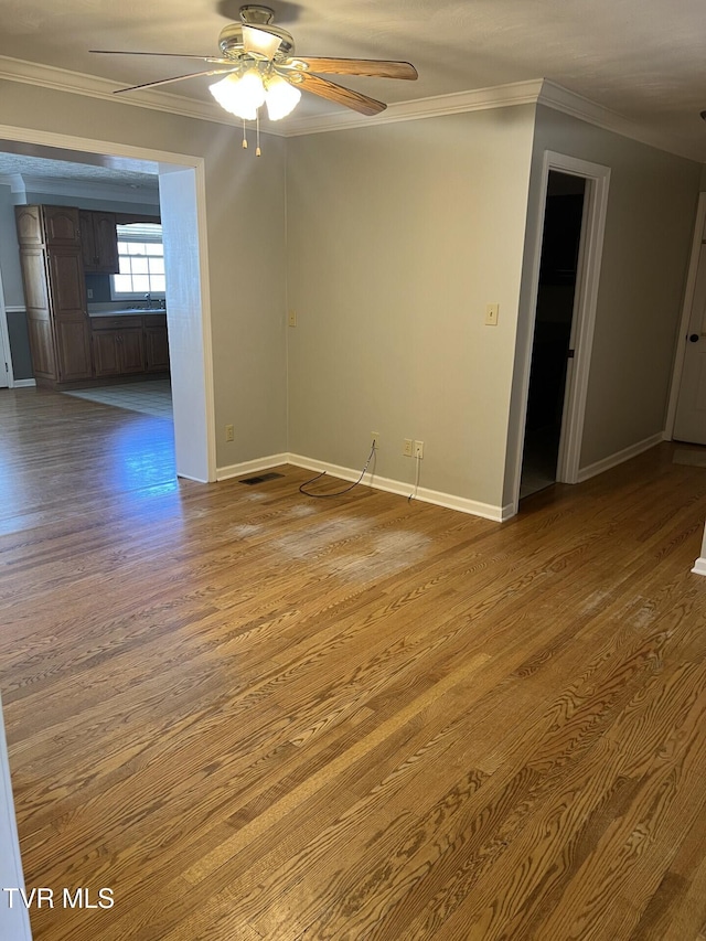 spare room featuring ceiling fan, baseboards, crown molding, and wood finished floors