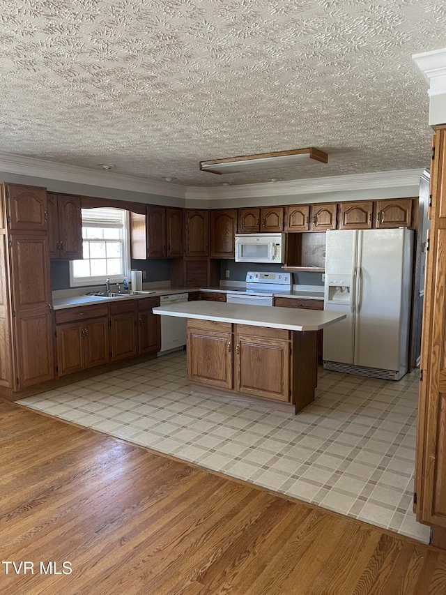 kitchen featuring white appliances, a center island, light countertops, light wood-type flooring, and a sink