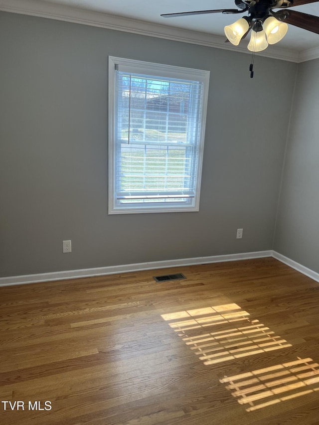 unfurnished room with crown molding, visible vents, a ceiling fan, wood finished floors, and baseboards