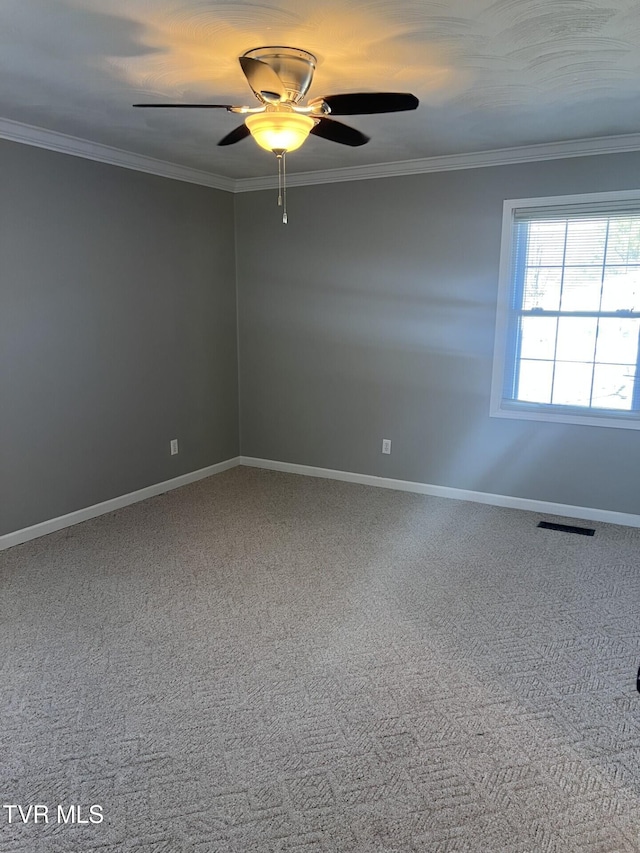 spare room featuring ceiling fan, visible vents, baseboards, ornamental molding, and carpet