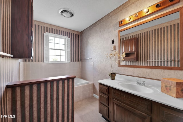 bathroom featuring vanity, a textured ceiling, and tiled bath