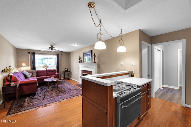 kitchen with black stove, hanging light fixtures, ceiling fan, light wood-type flooring, and a textured ceiling