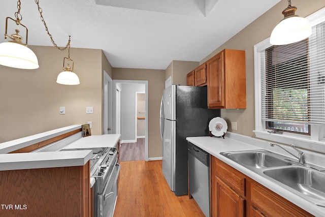 kitchen featuring appliances with stainless steel finishes, a textured ceiling, sink, pendant lighting, and light hardwood / wood-style flooring