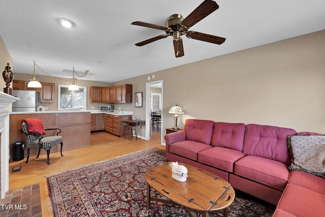 living room featuring ceiling fan, light wood-type flooring, and a textured ceiling