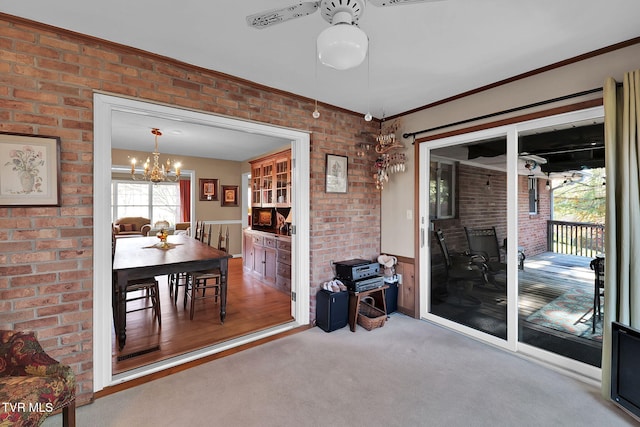 carpeted dining room with ceiling fan with notable chandelier, crown molding, and brick wall