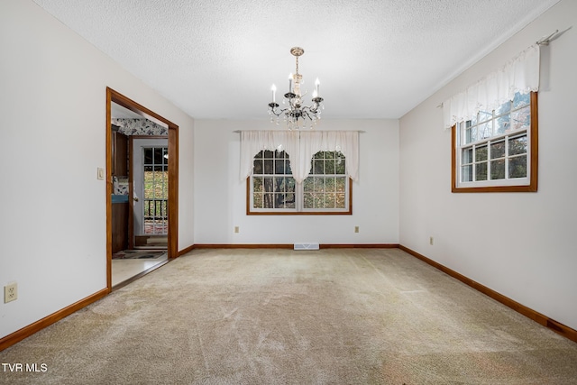 spare room with a textured ceiling, carpet floors, and a notable chandelier