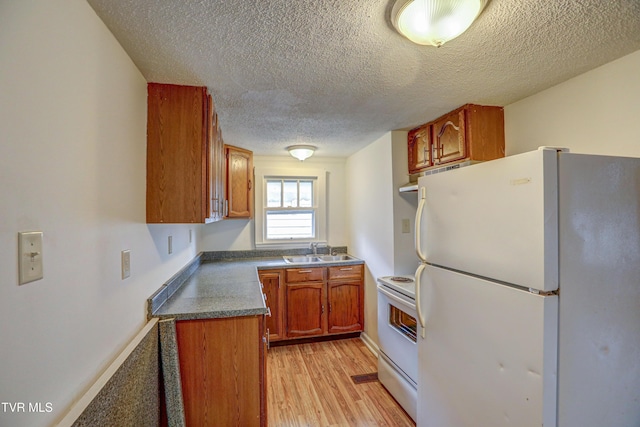 kitchen with a textured ceiling, sink, white appliances, and light wood-type flooring