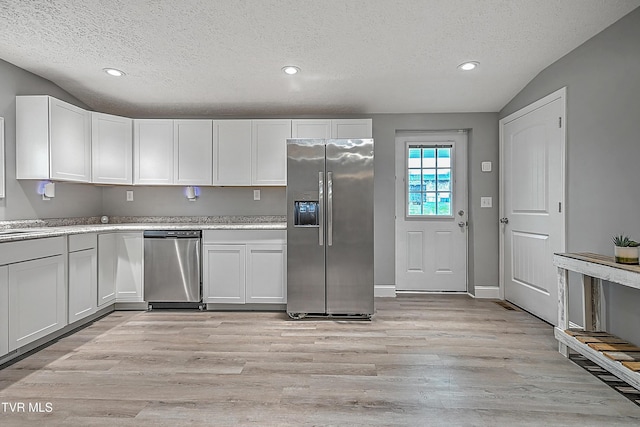 kitchen featuring appliances with stainless steel finishes, a textured ceiling, vaulted ceiling, white cabinets, and light hardwood / wood-style floors