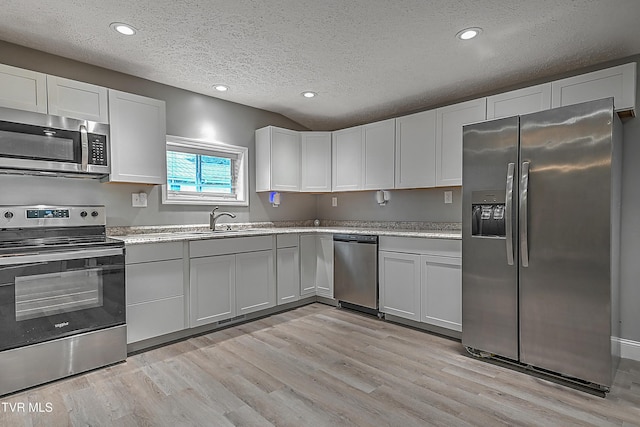 kitchen with a textured ceiling, stainless steel appliances, sink, light hardwood / wood-style flooring, and white cabinets