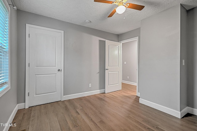 unfurnished bedroom with a textured ceiling, light wood-type flooring, and multiple windows