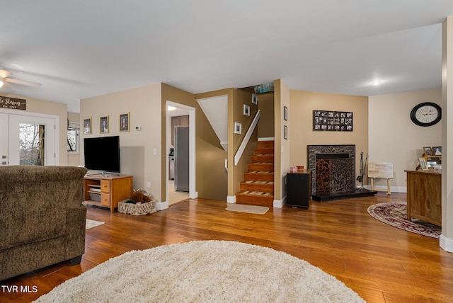 living room with a stone fireplace, ceiling fan, and hardwood / wood-style floors