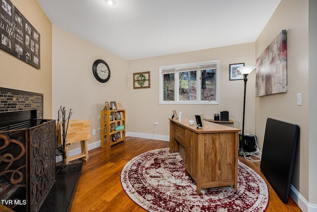 office with hardwood / wood-style flooring and a brick fireplace