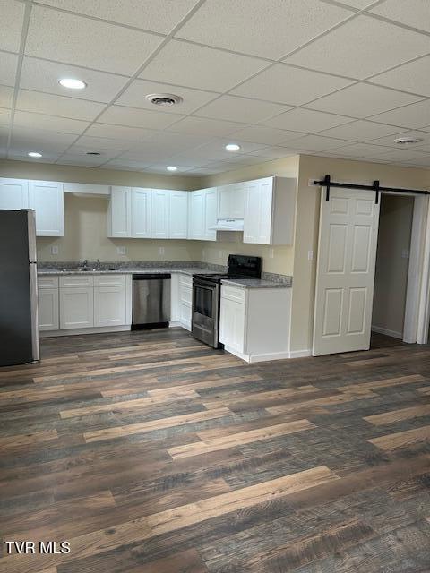 kitchen with white cabinets, dark hardwood / wood-style floors, a barn door, and appliances with stainless steel finishes