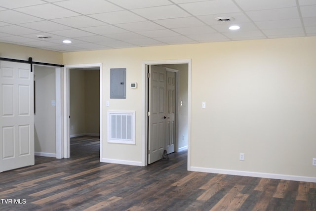 unfurnished room with a barn door, electric panel, a drop ceiling, and dark hardwood / wood-style floors