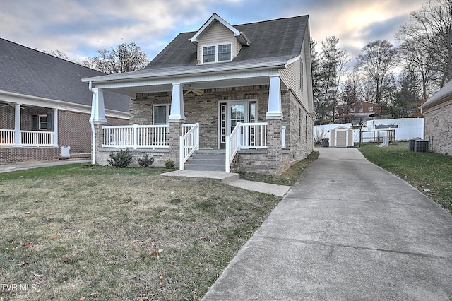 view of front of property with central AC unit, covered porch, a yard, and a shed