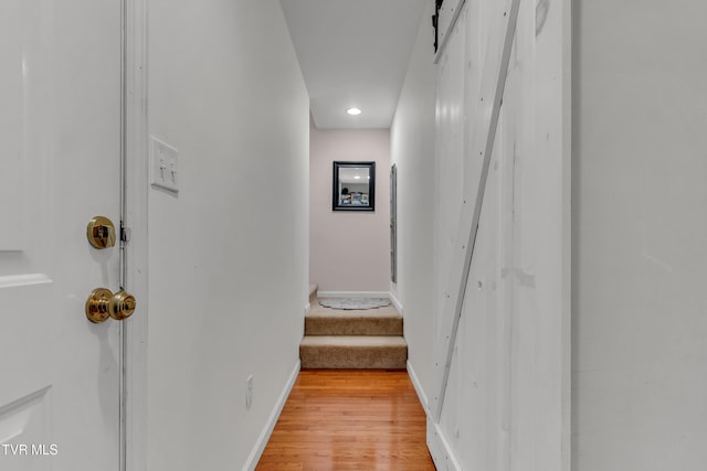 corridor with light wood-type flooring and a barn door