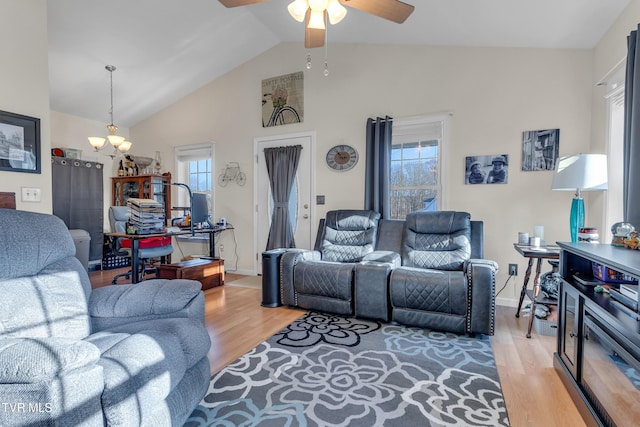 living room with ceiling fan with notable chandelier, light hardwood / wood-style floors, and high vaulted ceiling