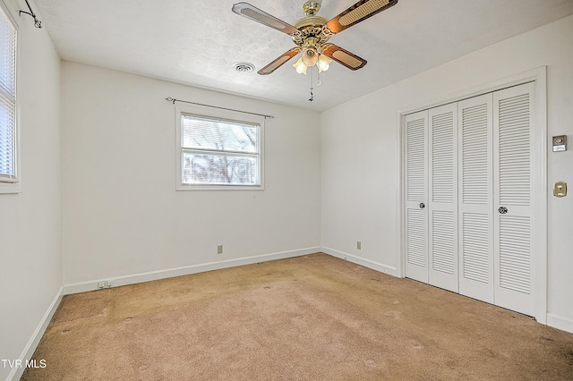 unfurnished bedroom featuring light carpet, a textured ceiling, a closet, and ceiling fan