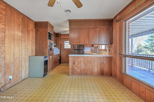 kitchen featuring ceiling fan, sink, stainless steel appliances, kitchen peninsula, and wood walls