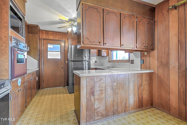 kitchen with kitchen peninsula, a textured ceiling, sink, black appliances, and wood walls