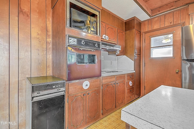 kitchen featuring oven, range hood, built in microwave, and stainless steel refrigerator