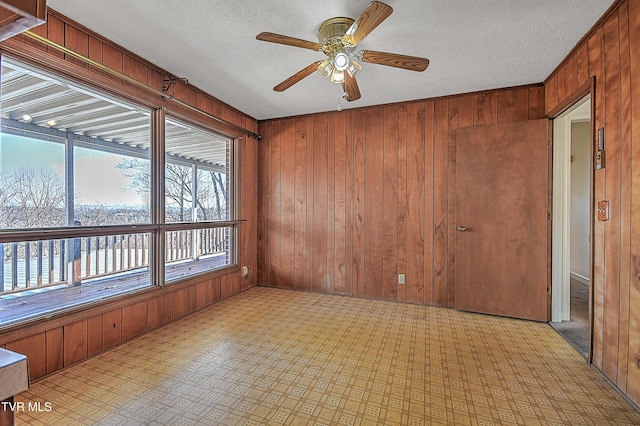 unfurnished room with ceiling fan, wood walls, and a textured ceiling