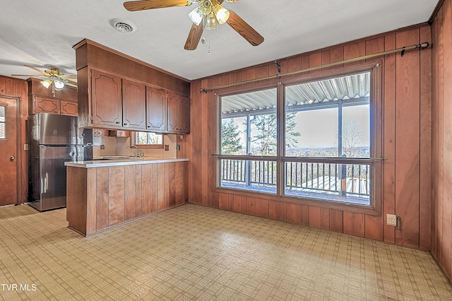 kitchen featuring ceiling fan, wood walls, kitchen peninsula, and stainless steel refrigerator