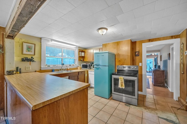 kitchen with wood walls, kitchen peninsula, sink, and appliances with stainless steel finishes