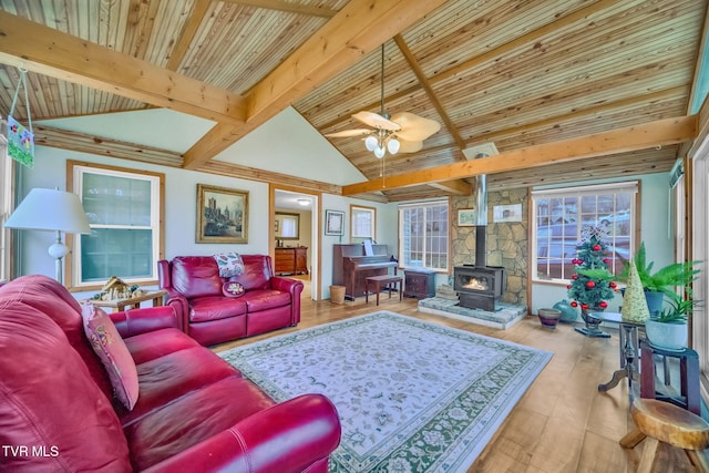 living room featuring lofted ceiling with beams, ceiling fan, light wood-type flooring, and a wood stove