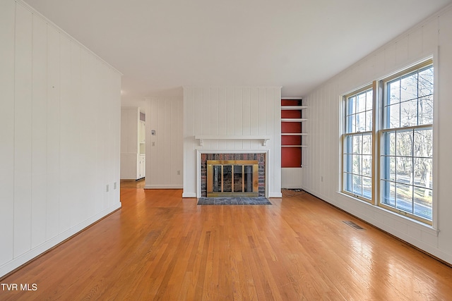 unfurnished living room with a fireplace, wood walls, light hardwood / wood-style flooring, and ornamental molding